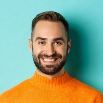 happy-handsome-man-writing-message-on-mobile-phone-holding-smartphone-and-smiling-standing-against-e1627382629858.jpg